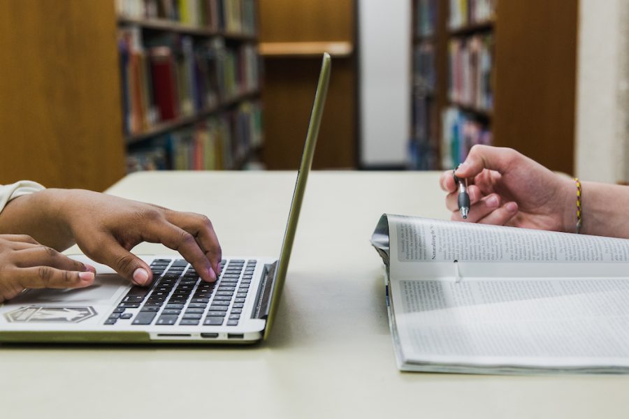 two students studying in the library, one reading and one on a laptop